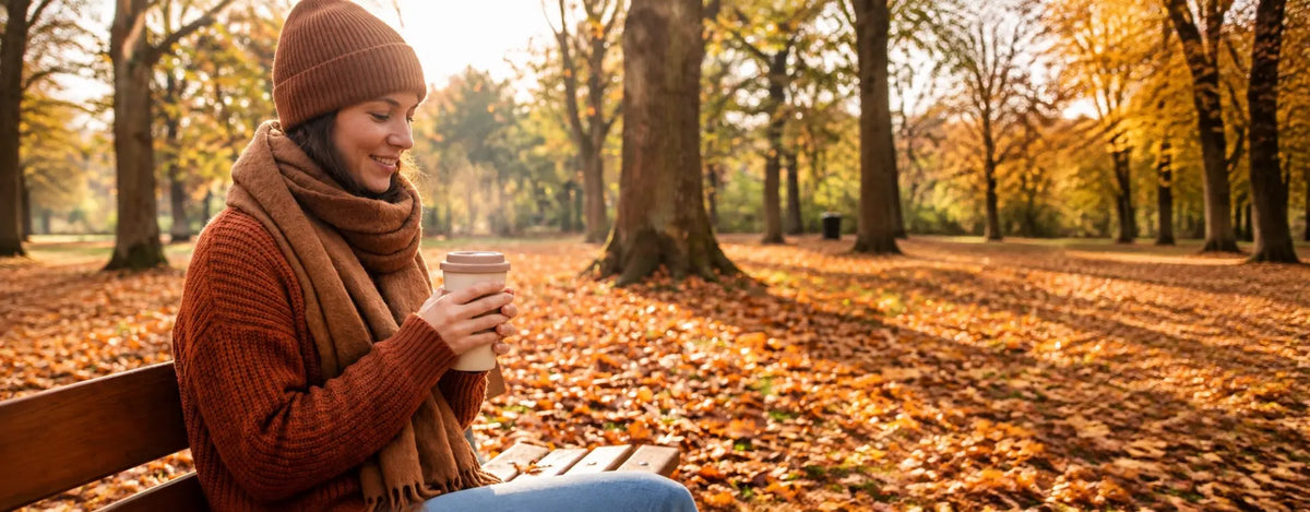 Frau in warmer Kleidung mit heißem Getränk im Herbstpark, Symbolbild für Immunsystem und kalte Jahreszeit