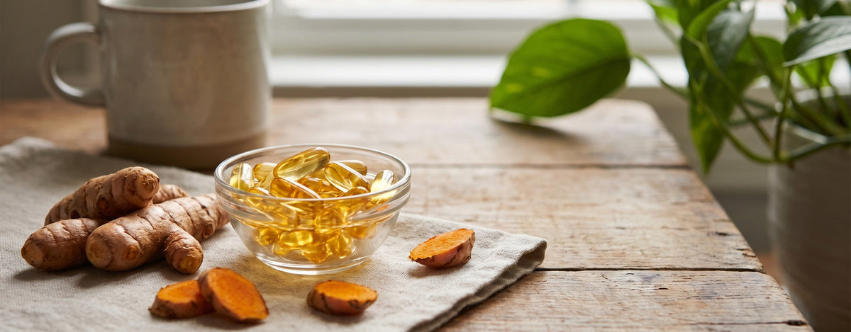 Fischölkapseln und Kurkumawurzel nebeneinander auf einem Tisch, Symbolbild für Omega-3 und Curcumin im Vergleich